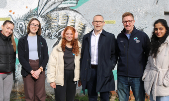Staff and students line up in front of  wall with insect mural