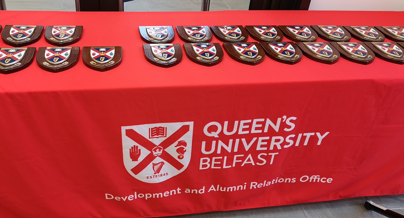 Call for nominations! Multiple plaques of Queen's University Belfast crest on a University branded red tablecloth