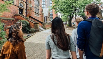 Five students, backs to camera, looking at University building with pathway in front of them