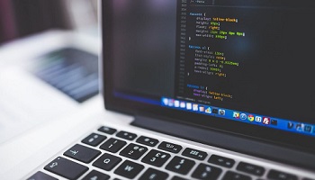 Desktop computer keyboard and screen showing coding