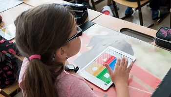 Young schoolgirl (with her back to camera) working at an iPad, sitting behind desk in classroom
