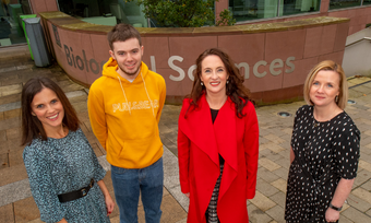 Four people standing in front of wall with sign saying 'Biological Sciences'